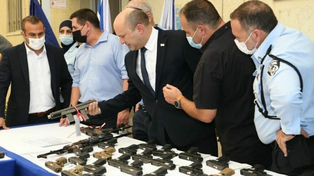 Premier Bennet betrachtet im Rahmen der "Operation Sword Strike" konfiszierte Waffen