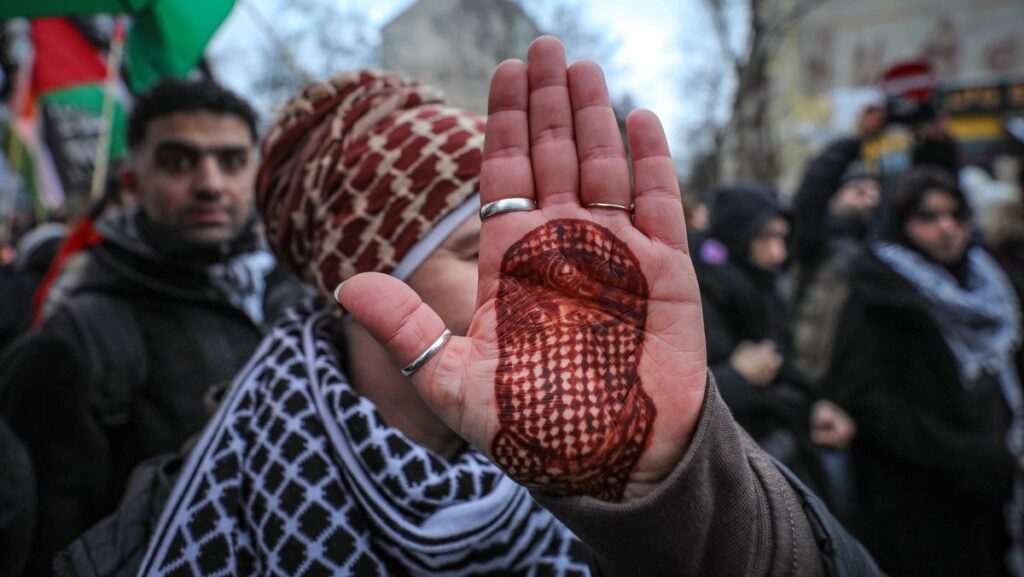 Demonstrantin in Berlin mit Bild des Hama-Militärsprechers Abu Obaida auf ihrer Hand