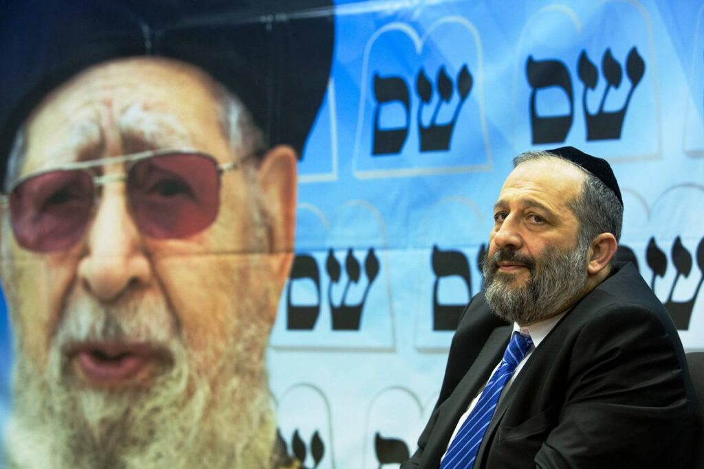 Der langjährige Schas-Politiker Aryeh Deri vor einem Bild von Rabbi Ovadia Yosef. (© imago images/Xinhua)